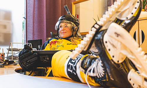 Kvinna iklädd hockeyutrustning sitter vid sitt skrivbord på banken.